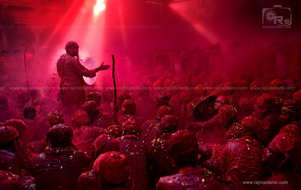 Travel photojournalism of Indian woman celebrating Holi festival with face and sari covered in vibrant red colors by Rajiv Solanki